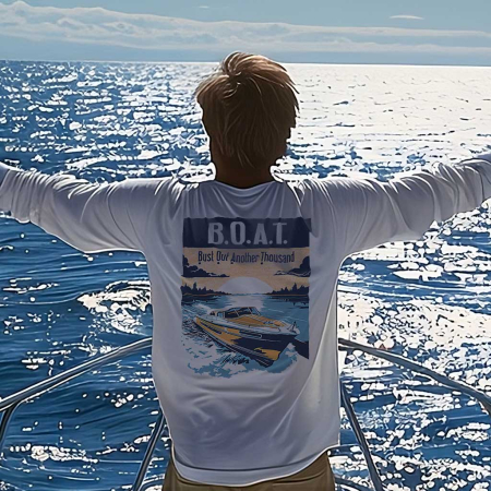 A man stands with arms wide open aboard a boat, facing the glistening ocean. He's wearing a white long-sleeve T-shirt that features a vintage design with the acronym 'B.O.A.T.' and the phrase 'Bust Out Another Thousand', along with an image of a classic speedboat. The shirt humorously refers to the high maintenance cost of boats, and the individual's posture expresses freedom and a deep connection with the sea, embodying the spirit of boating